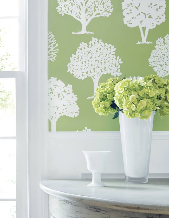 Decorative wall with tree pattern, table with flowers and vase, and window in the background