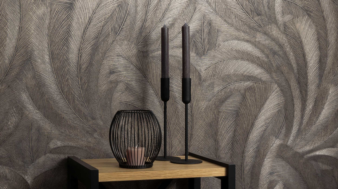 Erismann Elysium botanical feather wallpaper in deep charcoal and metallic taupe tones, styled as a feature wall behind a console table with decorative candles and accents, creating a moody and sophisticated atmosphere with rich texture and subtle shimmer.slider_item_ggh4Re