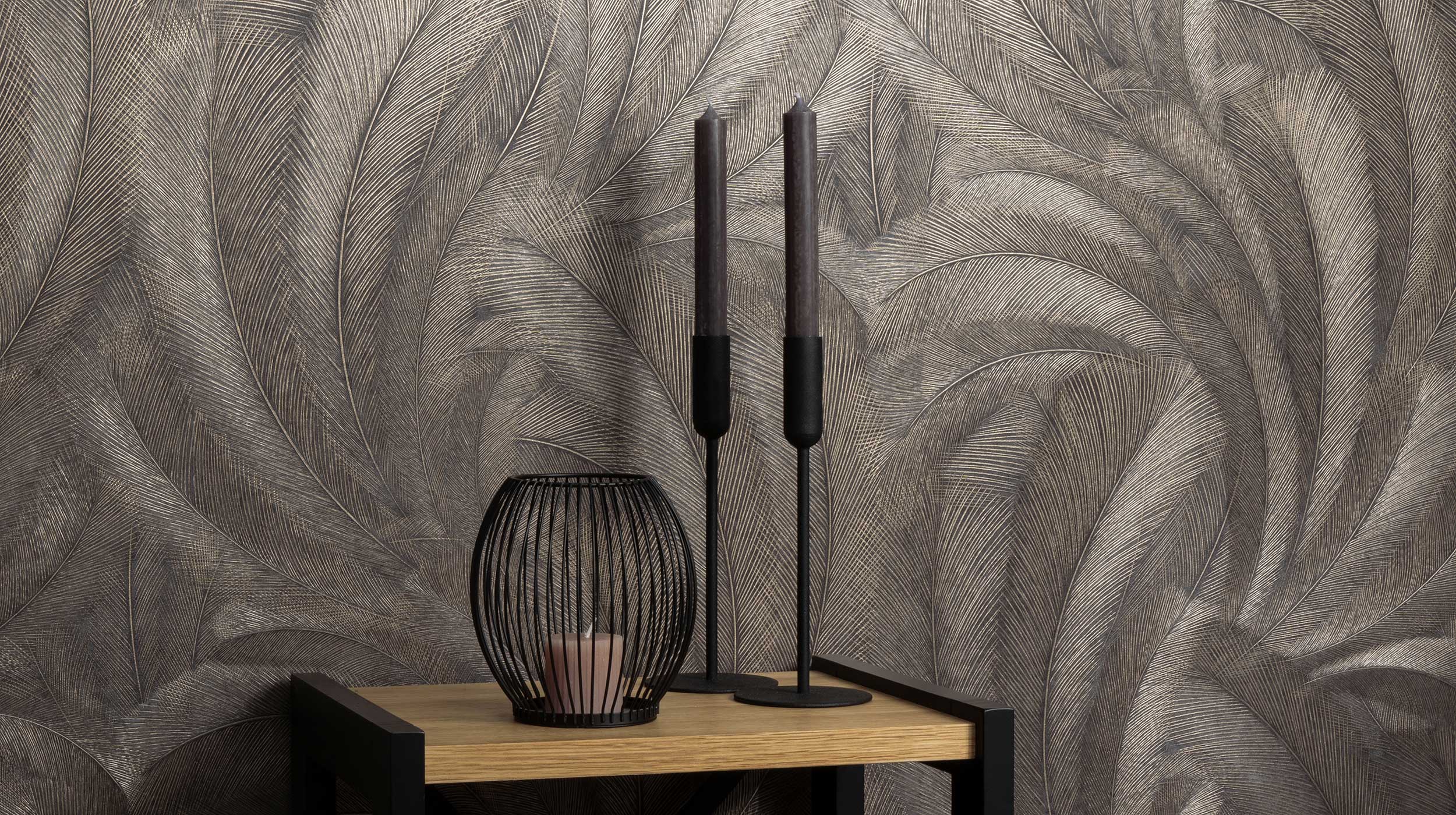 Erismann Elysium botanical feather wallpaper in deep charcoal and metallic taupe tones, styled as a feature wall behind a console table with decorative candles and accents, creating a moody and sophisticated atmosphere with rich texture and subtle shimmer.slider_item_ggh4Re
